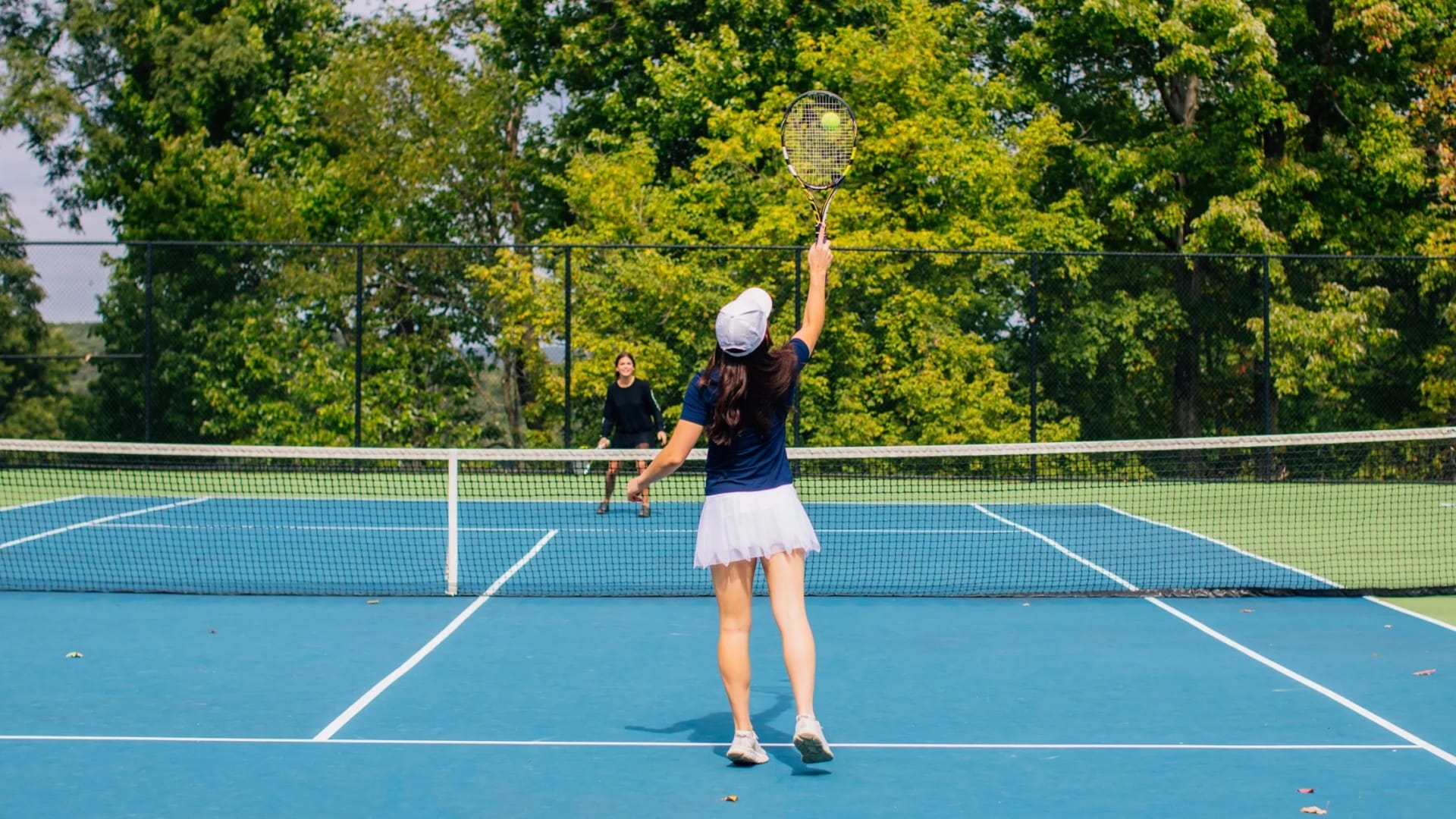 Pristine tennis courts at a luxury hotel resort with players in action, surrounded by lush landscaping and VIP seating.