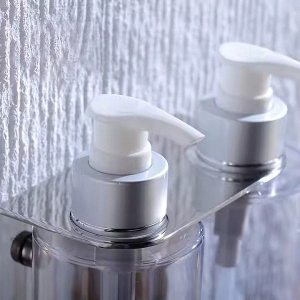 DERBAL triple-compartment soap dispenser wall-mounted in a hotel bathroom, rust-proof pump visible, with shampoo, conditioner, and body wash bottles for size comparison.