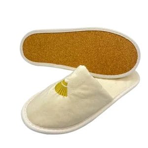 A pair of soft, white Cotton Cork Sole Slippers placed on a natural wood surface, highlighting its comfortable and eco-friendly design.