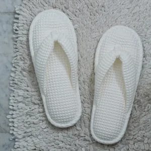 A pair of plush, white Waffle Slippers with a closed toe, elegantly placed on a hotel room floor, emphasizing luxury and comfort.