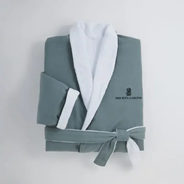A guest looking comfortable and relaxed while wearing the beige Luxury Hotel Bathrobe, sitting in a well-lit, luxurious hotel room setting.