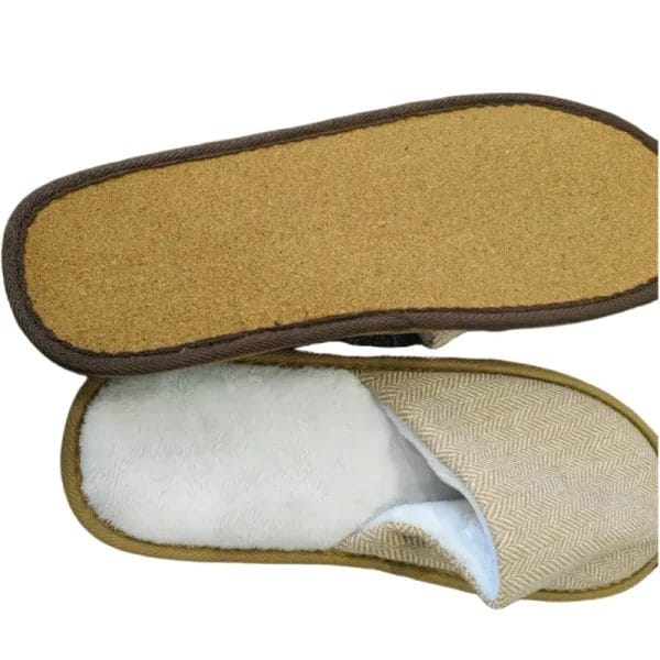 An artistic flat-lay showing the Hotel Eco-friendly Slipper surrounded by its raw materials, including a piece of cork bark and a swatch of linen fabric.