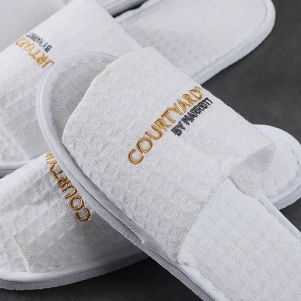 A shot of a new, disposable pair of Waffle Slippers neatly presented in a spa or resort setting, ready for guest use.
