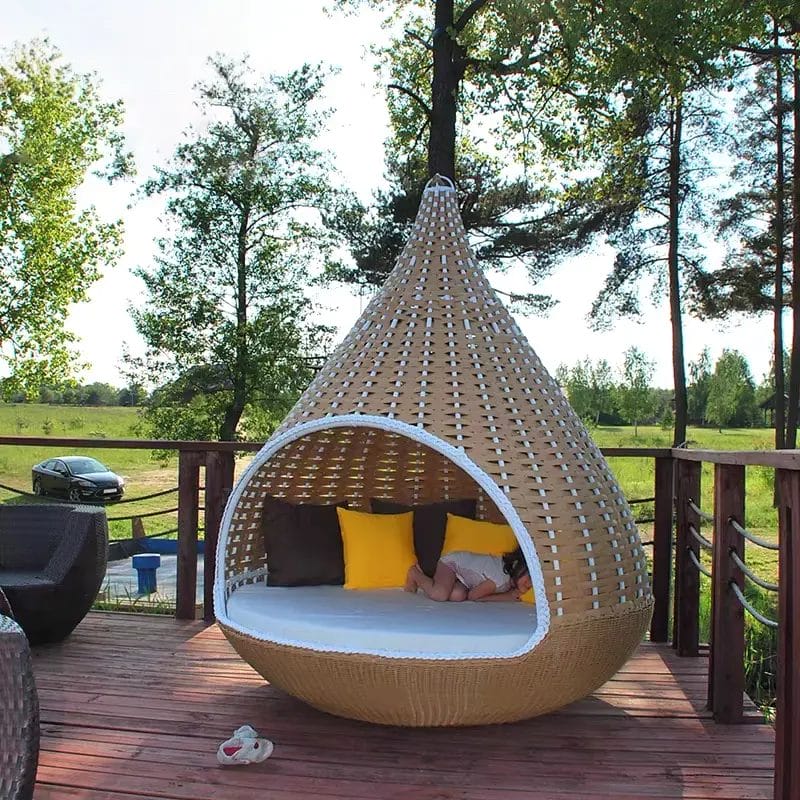 A stylish, single-person Outdoor Rattan Hanging Chair suspended on a modern hotel room balcony, creating an inviting and highly 'Instagrammable' private reading nook.