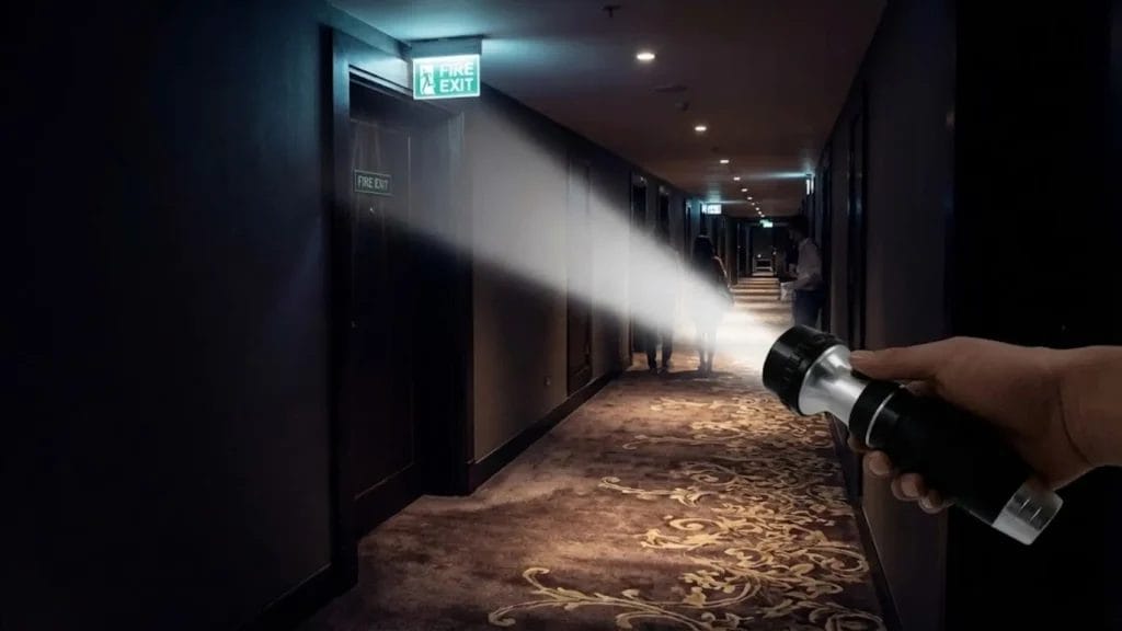 A guest uses a bright Hotel Emergency torch to illuminate a dark hotel corridor, highlighting a fire exit sign during a power failure.
