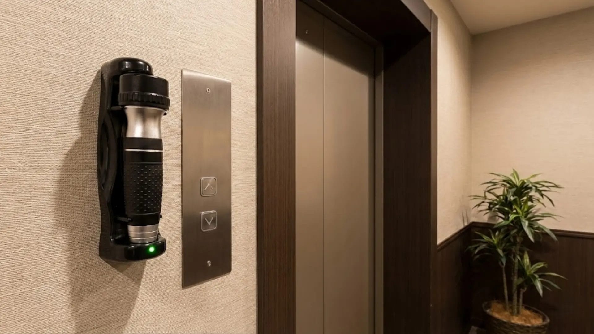 A Hotel Emergency torch and charging base mounted on the wall of a modern hotel elevator lobby, ready for use next to the elevator call buttons.