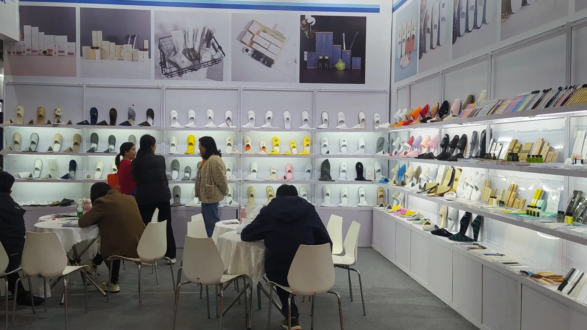 The busy DERBAL booth at the 31st Guangzhou Hotel Equipment Exhibition, featuring a large display wall of hotel slippers and clients discussing full-room solutions.