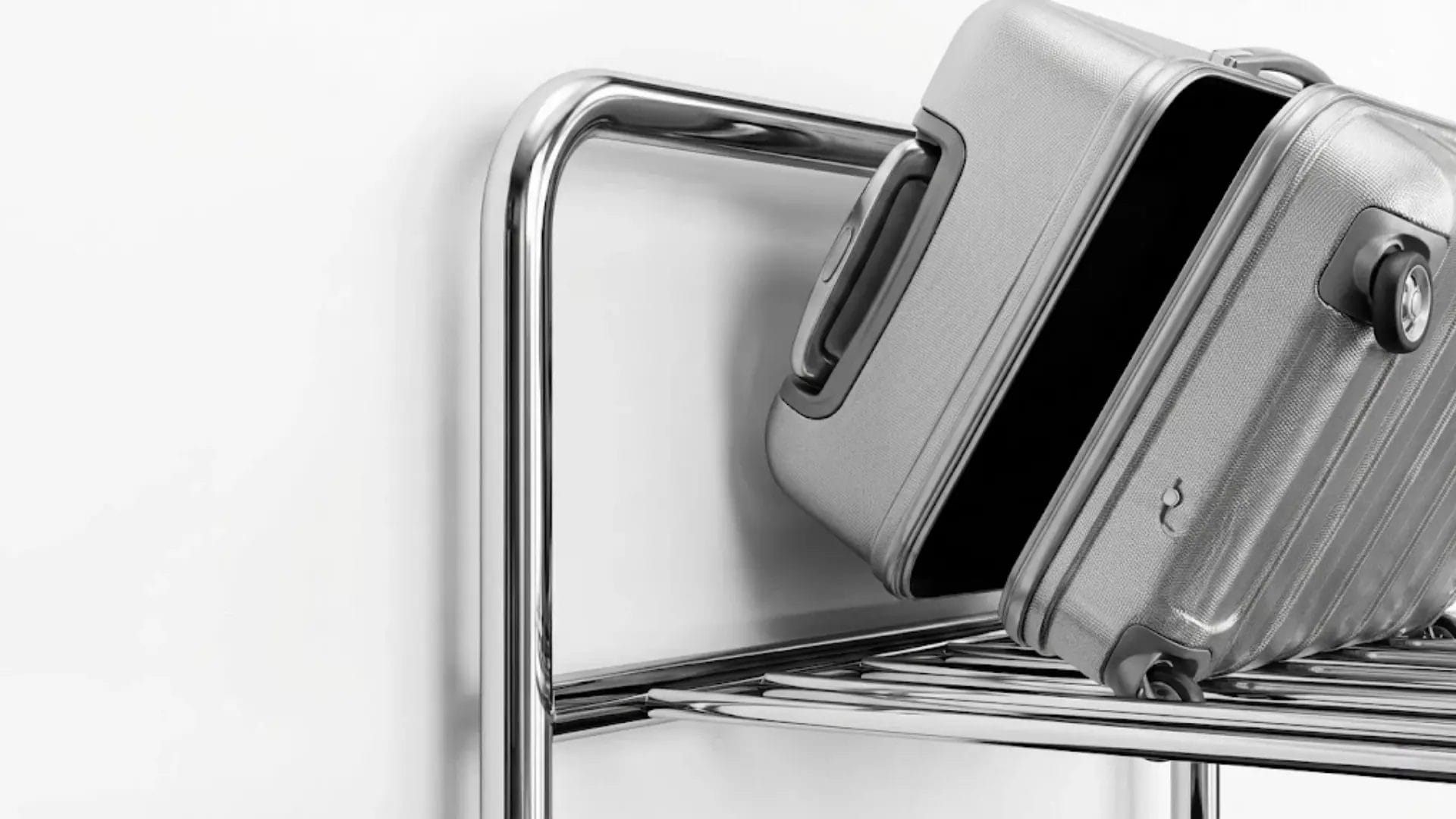 Chrome hotel luggage rack with wall guard preventing suitcase from scratching the wall.