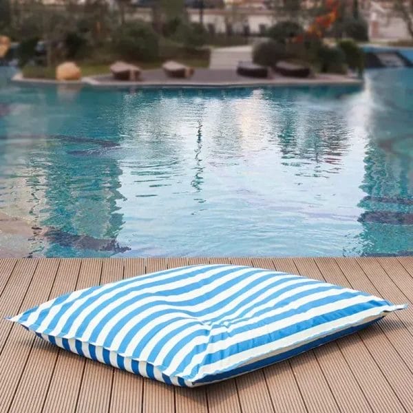 A blue and white horizontal striped bean bag chair sitting on a wooden pool deck overlooking a swimming pool.