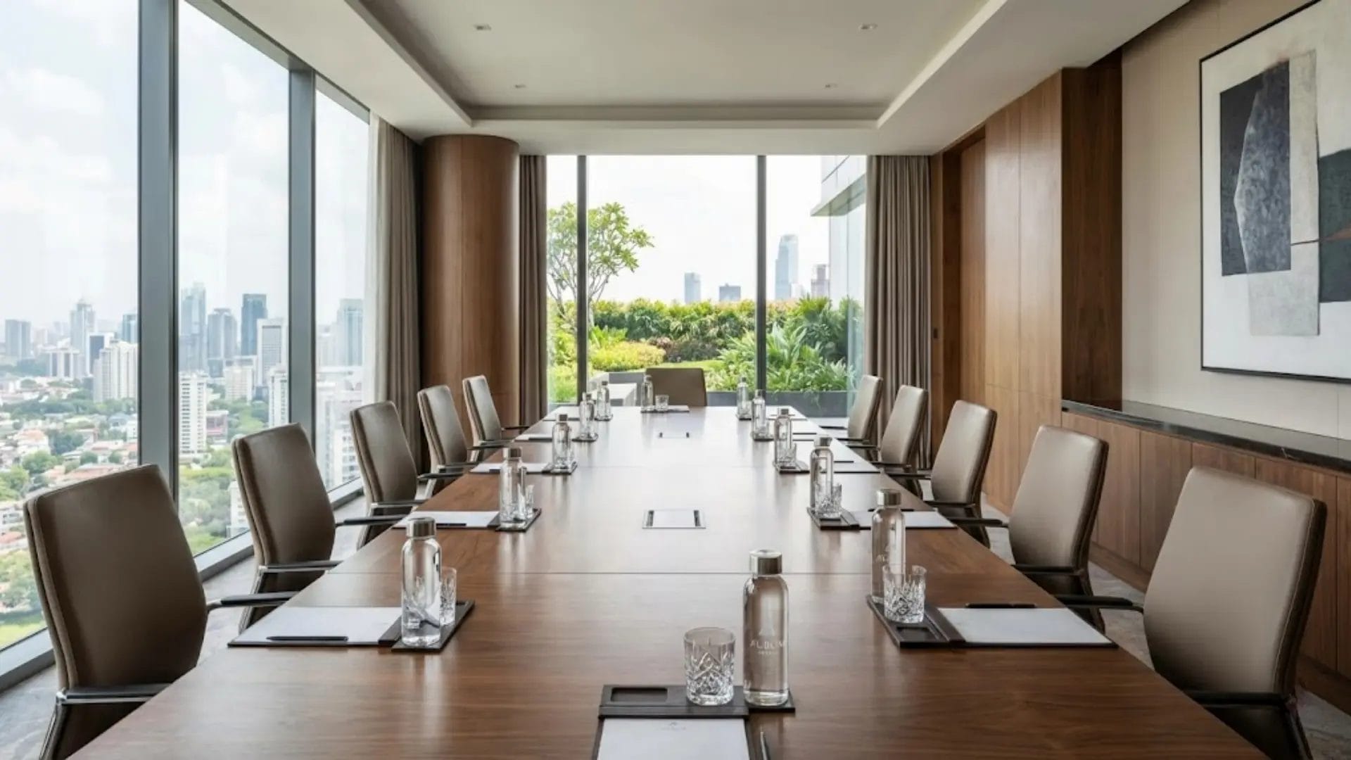 A luxury hotel conference room with a long wooden table set with custom glass water bottles and crystal glasses for a meeting.