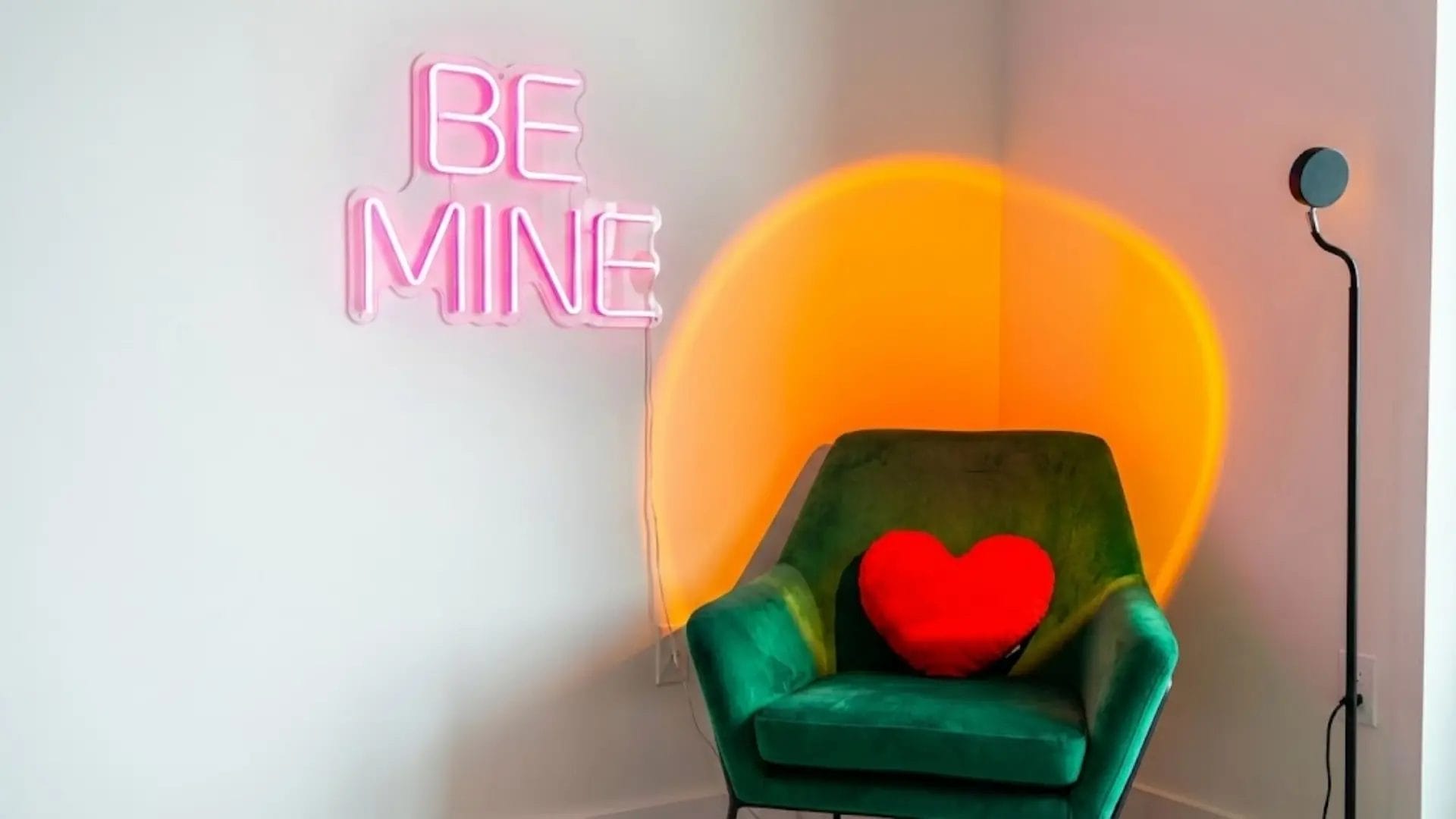 Hotel room corner with glowing pink BE MINE neon sign and warm sunset lamp for photos