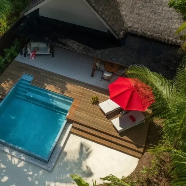 Red sun protection umbrella at a hotel poolside with two luxury sun loungers.