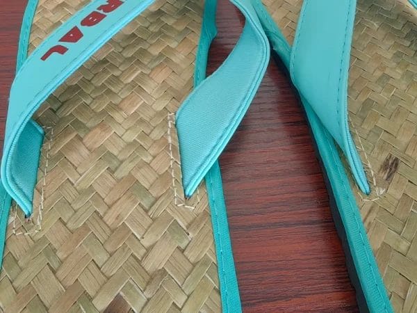 A pair of natural Raffia Straw Flip Flops resting on a teak wooden deck next to a luxury resort infinity pool.